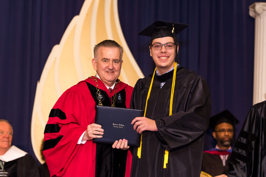 A man in graduation gown and cap standing next to another person.